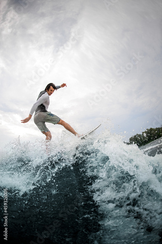 Active sportsman skilfully balancing on wave on wakesurf board.