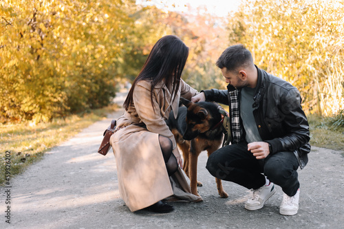 Happy young family a man and a woman in love have fun walking with their dog pet in a fall park in nature in autumn outdoor, selective focus