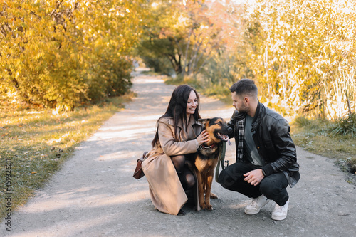 Happy young family a man and a woman in love have fun walking with their dog pet in a fall park in nature in autumn outdoor, selective focus