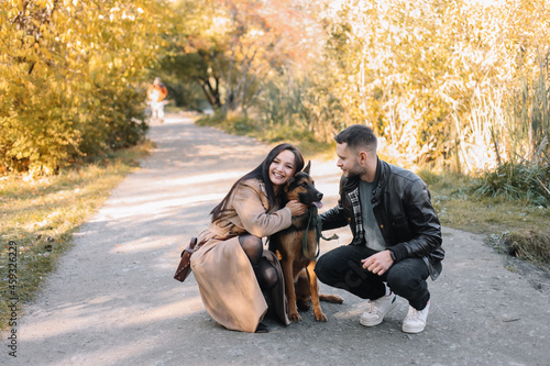 Happy young family a man and a woman in love have fun walking with their dog pet in a fall park in nature in autumn outdoor, selective focus