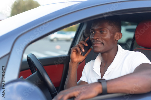 An African-American man sitting behind the wheel of a car with a phone in his hand