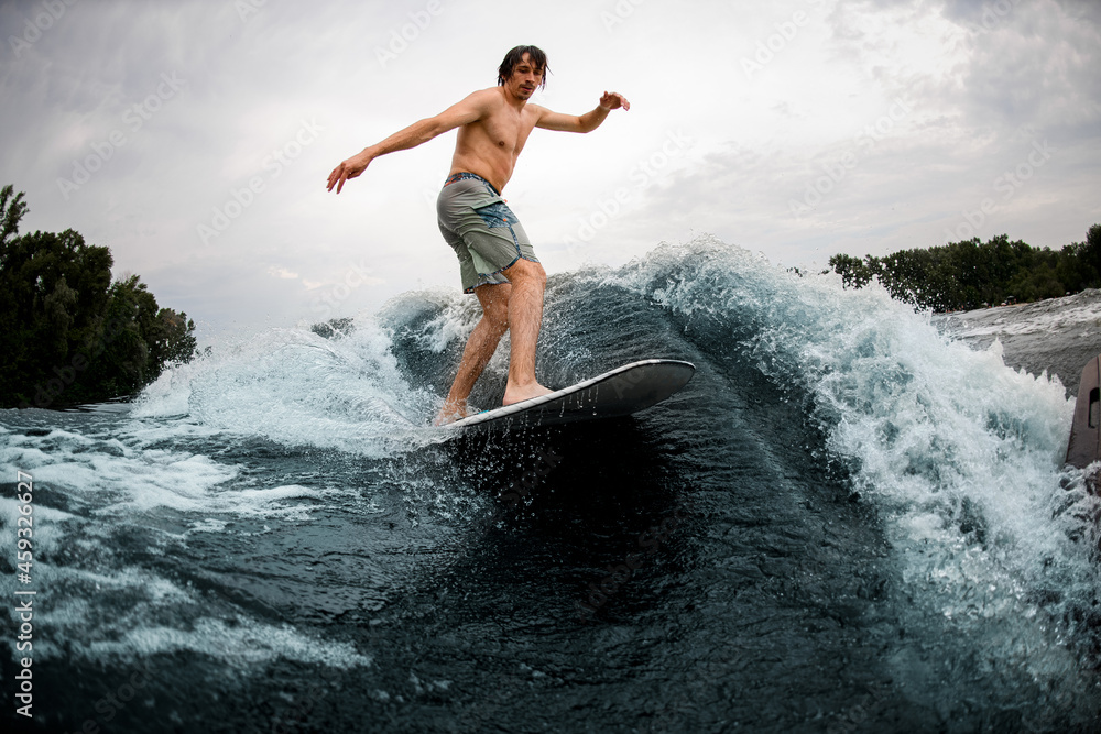 active sportive man rides down the wave on wakesurf board.