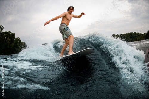 active sportive man rides down the wave on wakesurf board.