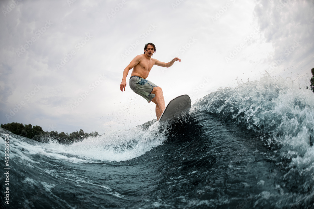 energetic man go in for active water sport and ride the wave on wakesurf board