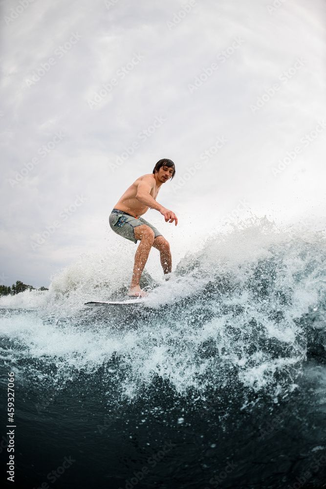Fototapeta premium Young energetic man go in for active water sport and ride the wave on wakeboard