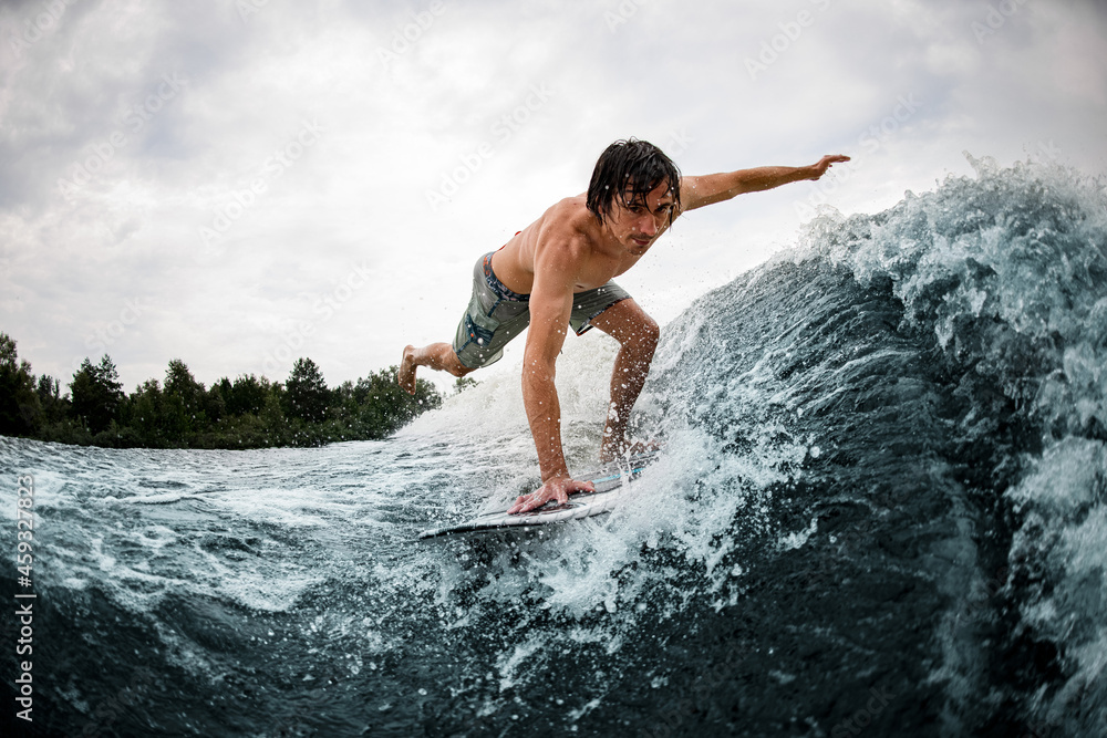 man balancing on wake surf board on wave with stretching his leg and hand