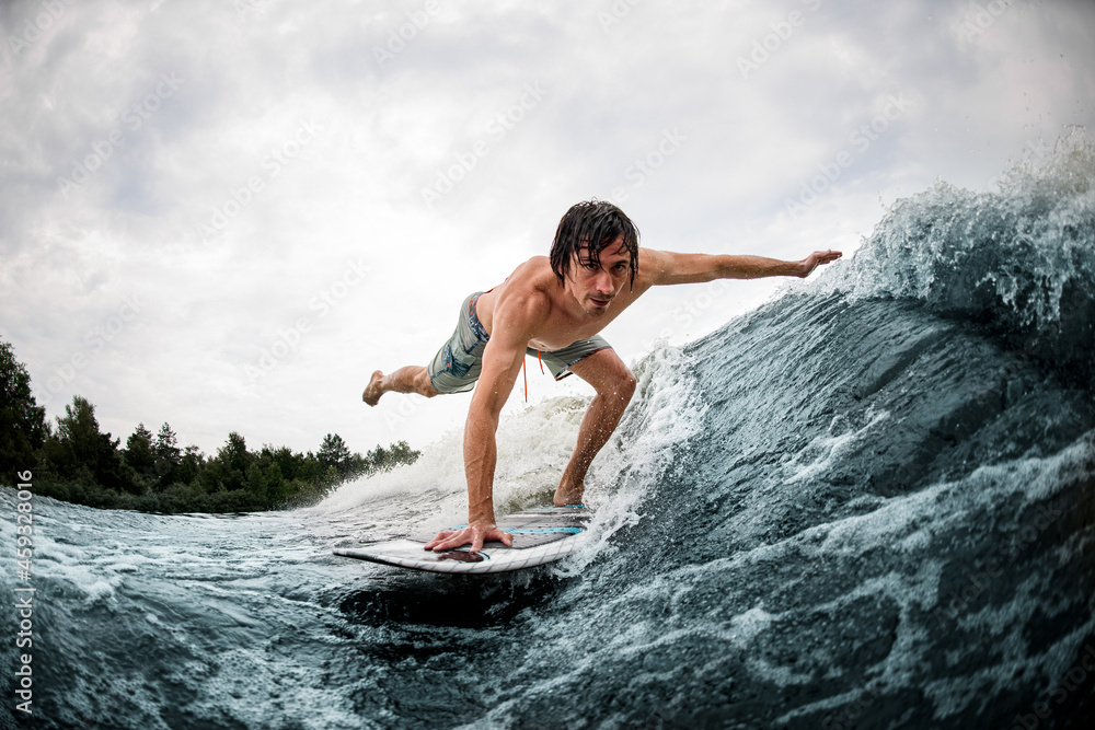 athletic man make trick balancing on wake surf board on wave with stretching his leg and hand