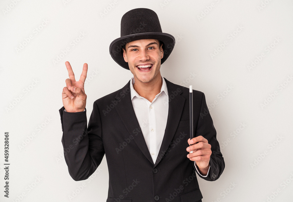 Young magician caucasian man holding a wand isolated on white background joyful and carefree showing a peace symbol with fingers. Young magician caucasian man holding a wand isolated on white background joyful and carefree showing a peace symbol with fingers.