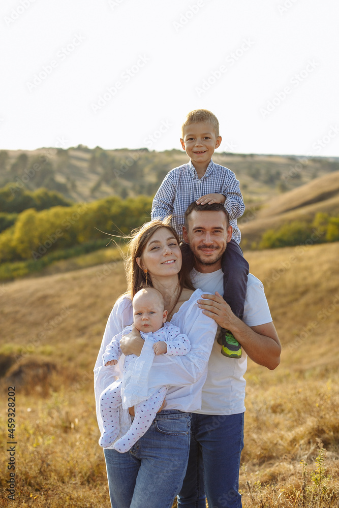 mom dad and two sons posing on the background of nature in a field with tall grass