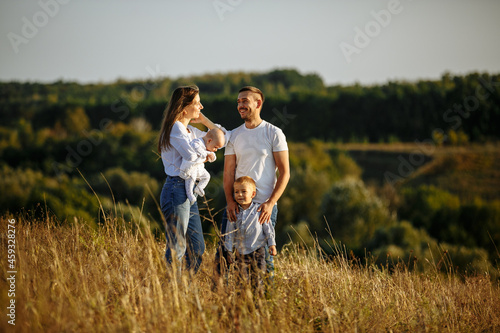 mom dad and two sons posing on the background of nature in a field with tall grass