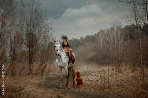 Little girl in riding habit with horse and vizsla in spring forest
