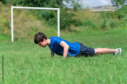 teenage boy exercising outdoors, sports ground in the yard, he does push-ups on the soccer field, healthy lifestyle