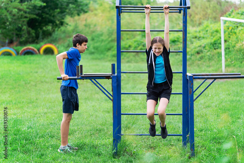 teenage boy and girl exercising outdoors, sports ground in the yard, they posing at the horizontal bar, healthy lifestyle