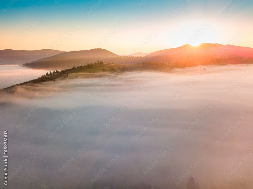 Fog spreads over the mountains at dawn. The sun rises on the horizon. Ukrainian Carpathians in the morning. Aerial drone view.