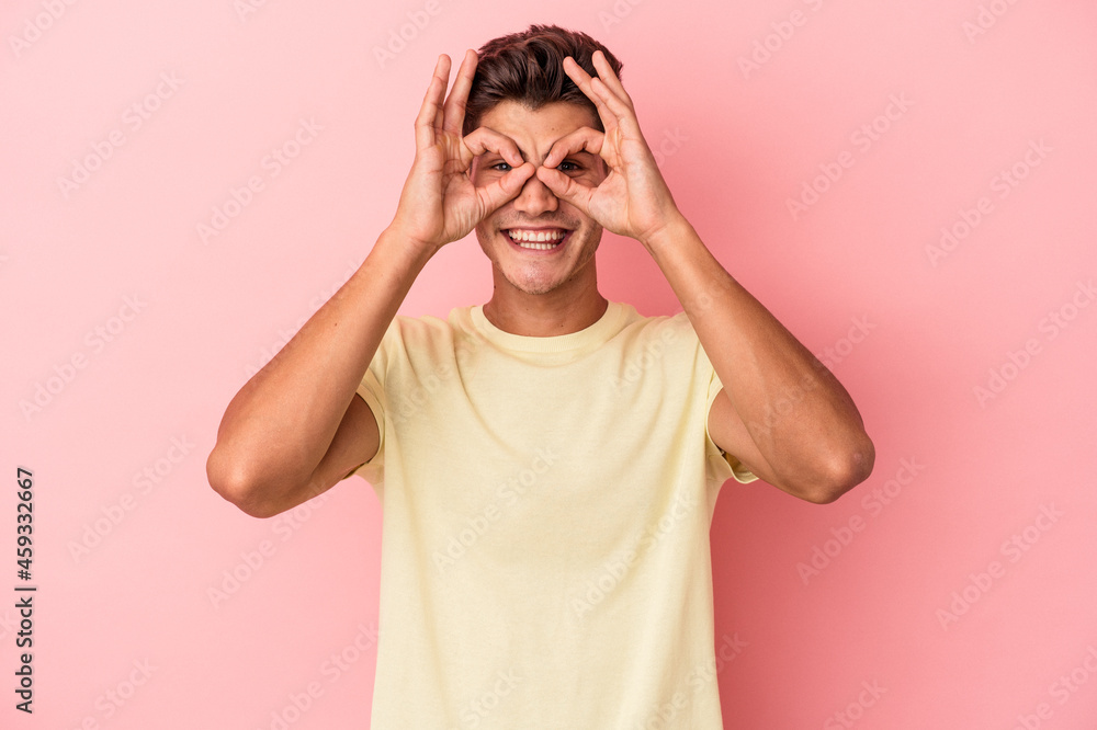 Young caucasian man isolated on pink background showing okay sign over eyes Young caucasian man isolated on pink background showing okay sign over eyes
