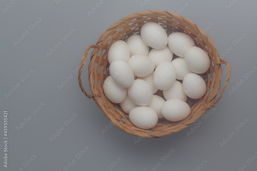 White chicken eggs in a brown wicker basket on a gray background White chicken eggs in a brown wicker basket on a gray background