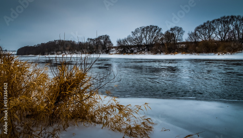 Winter landscape with an unfrozen river and vegetation along the banks