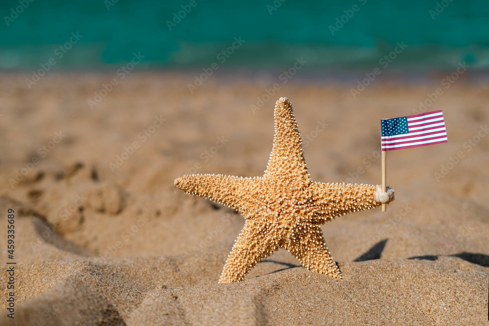 A starfish holds an American flag on the seashore. Labor day holiday concept. 4th of July USA Independence Day. Copy space for text. A starfish holds an American flag on the seashore. Labor day holiday concept. 4th of July USA Independence Day. Copy space for text.