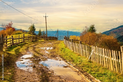 A path along the ridge of a hill with a large puddle and an old fence against the backdrop of a colorful forest