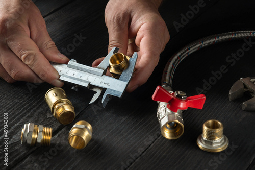 Professional wizard measures the size of fitting using a caliper before connecting water or gas pipe. Close-up of the hands of the master plumber. photo