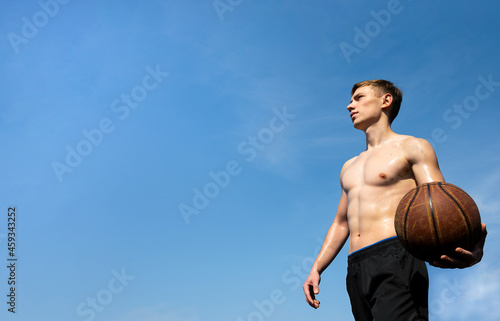 muscular young sportsman with basketball ball outdoors against sky background