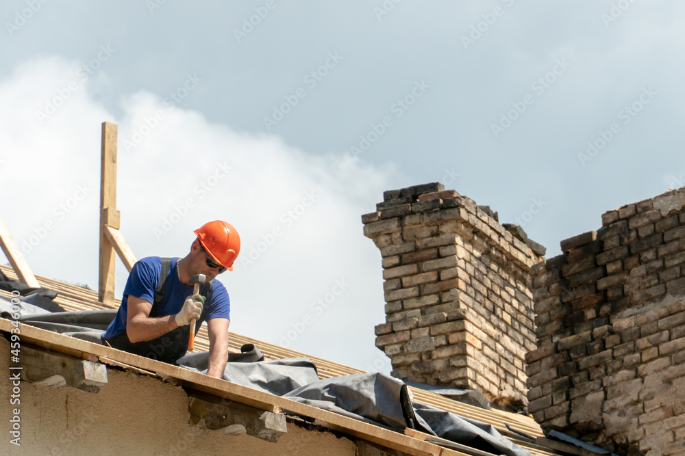 Repair of a wooden roof outdoors on a summer day against the background of blue sky and clouds. A carpenter in special clothes and with a tool installs beams and wood boards. Repair of a wooden roof outdoors on a summer day against the background of blue sky and clouds. A carpenter in special clothes and with a tool installs beams and wood boards.