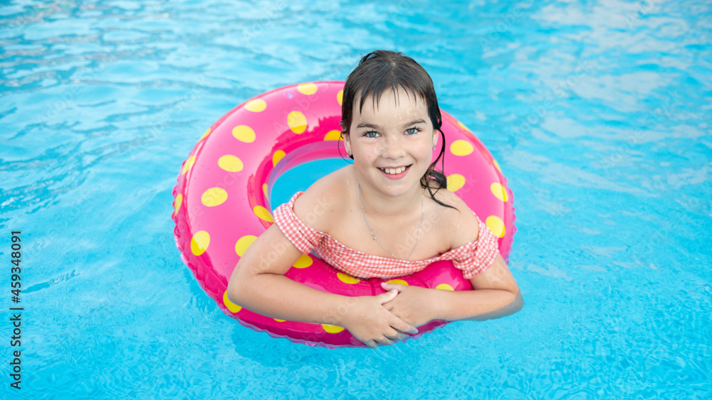 cute smiling girl in a bright circle swims on the background of a blue pool in summer. High quality photo