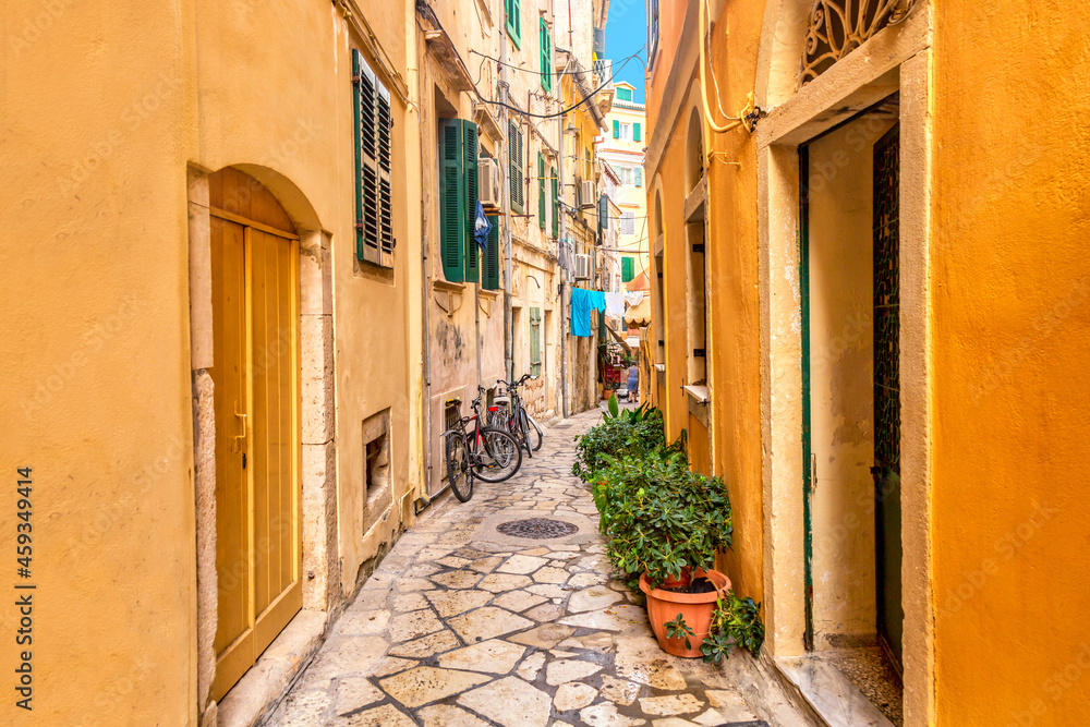 Kerkyra city narrow street view with yellow colorful houses and bikes during sunny day. Corfu Island, Ionian Sea, Greece.