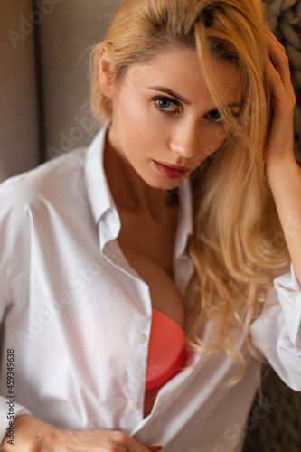 Sexy portrait of a pretty young woman with blonde hair in a white fashion shirt with a pink bra and beautiful breasts looking at the camera