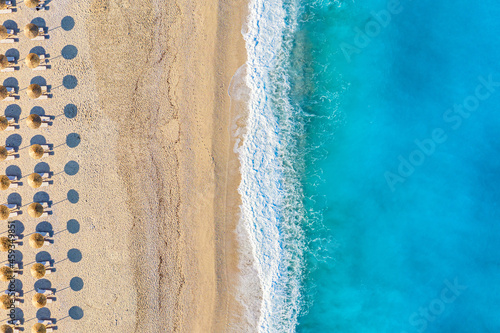 Top view aerial drone photo of Myrtos beach with beautiful turquoise water, sea waves and straw umbrellas. Vacation travel background. Ionian sea, Kefalonia Island, Greece