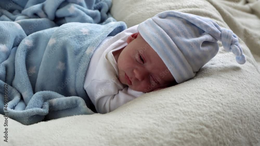 Close-up Newborn Baby Face Portrait Early Days Waking Up Open Eyes On Tummy Blue White Background. Child Start Minutes Of Life on Hat. Infants, Childbirth, First Moments Of Borning, Beginning Concept Close-up Newborn Baby Face Portrait Early Days Waking Up Open Eyes On Tummy Blue White Background. Child Start Minutes Of Life on Hat. Infants, Childbirth, First Moments Of Borning, Beginning Concept