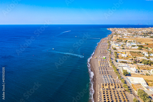 Top view aerial drone photo of black Perissa beach with beautiful turquoise water, sea waves and straw umbrellas. Vacation travel background. Aegean sea, Santorini Island, Greece photo