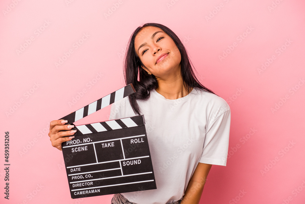 Young latin woman holding clapperboard isolated on pink background  dreaming of achieving goals and purposes