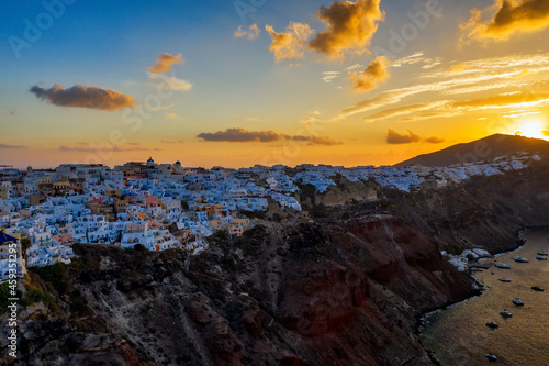 Aerial drone view of famous Oia village with white houses and blue dome churches during sunrise on Santorini island, Aegean sea, Greece.