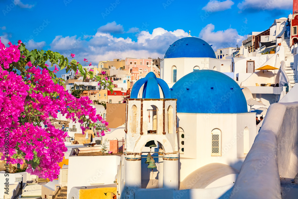 Famous Santorini view. Three blue domes and traditional white houses with bougainvillea flowers. Oia village, Santorini island, Greece.