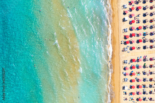 Top view aerial drone photo of Banana beach with beautiful turquoise water, sea waves and red umbrellas. Vacation travel background. Ionian sea, Zakynthos Island, Greece