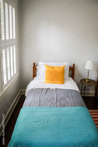 A guest bedroom with a single twin bed with turquoise and gray bedspread and yellow decorative pillow photo