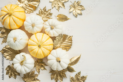 Sweet mini pumpkins and golden autumn leaves on a white wooden background with copy space. Thanksgiving day decor.