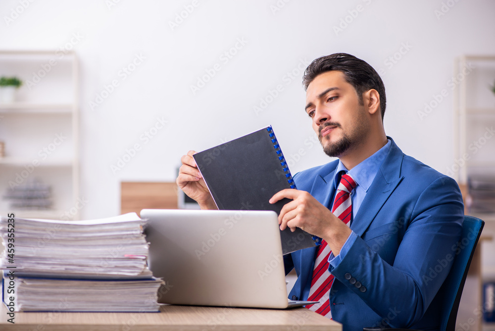 Young male employee unhappy with excessive work at workplace Young male employee unhappy with excessive work at workplace