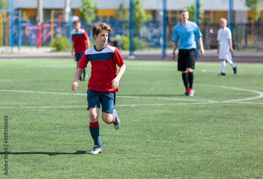 Teenager in red sportswear plays football on field, dribbles ball. Young soccer players with ball on green grass. Training, active lifestyle Teenager in red sportswear plays football on field, dribbles ball. Young soccer players with ball on green grass. Training, active lifestyle