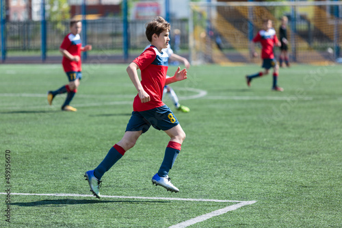 Teenager in red sportswear plays football on field, dribbles ball. Young soccer players with ball on green grass. Training, active lifestyle  © Natali