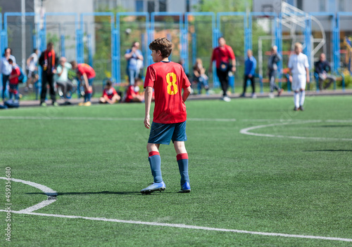 Teenager in red sportswear plays football on field, dribbles ball. Young soccer players with ball on green grass. Training, active lifestyle 