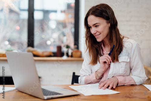 Woman doctor sitting at her desk, smiling and looking at her laptop screen