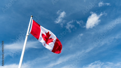 Canada flag pole waving in the wind under beautiful blue sky and clouds wallpaper. Canadian national red maple leaf symbol background