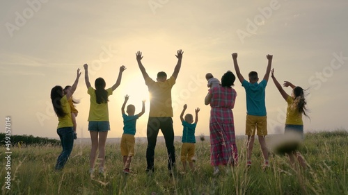 Happy big family rejoices and jumps raises hands with children on field in sunshine. People in park. Dad, mom with sons, daughter are walking outdoors. In summer, parents cheerful children have rest