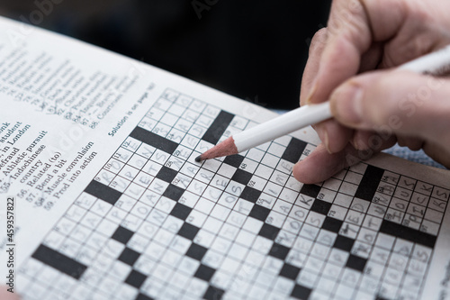 Solving a crossword puzzle in the newspaper close up hand background. Completing fun puzzle games hobby photo