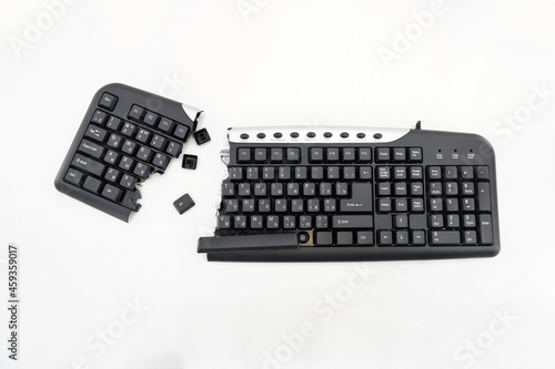 Broken keyboard. Destroyed keyboard. Black PC Keyboard is smashed and broken in half. With English and Russian keys, isolated on white background. Top view, close-up. Place for your text. photo