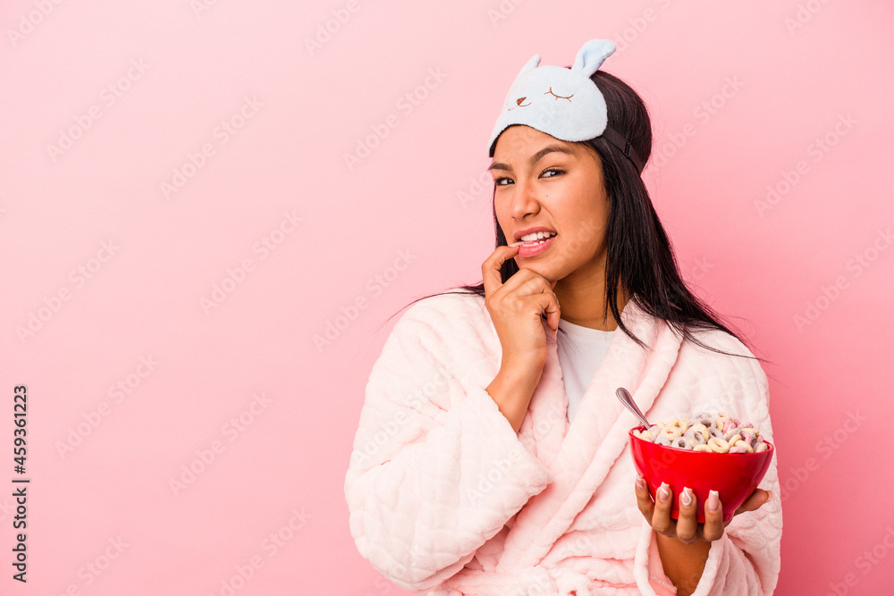 Young latin woman wearing pajama holding a bowl of cereals isolated on pink background relaxed thinking about something looking at a copy space. Young latin woman wearing pajama holding a bowl of cereals isolated on pink background relaxed thinking about something looking at a copy space.
