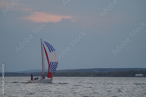 Full-color horizontal photo. A sports sailing vessel participates in a race in bad weather. Colored sails on the background of a stormy sky.