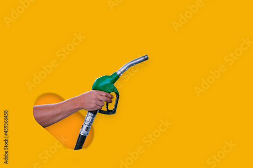 Man holds a refueling gun in his hand for refueling cars isolated on yellow background. Gas station with diesel and gasoline fuel close-up.